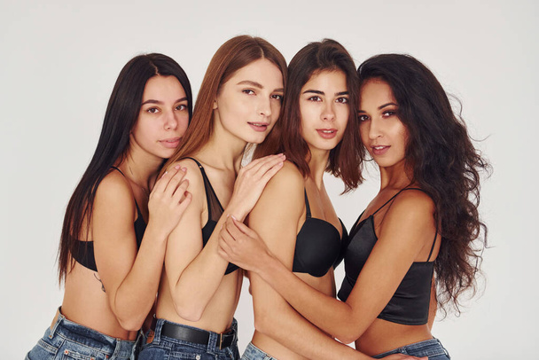 Leaning on each other. Four young women in lingerie together indoors. White background. - Photo, image