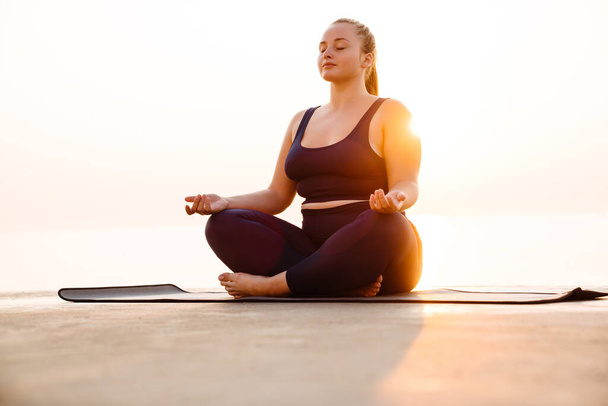 Ginger young woman meditating during yoga practice outdoors - 写真・画像