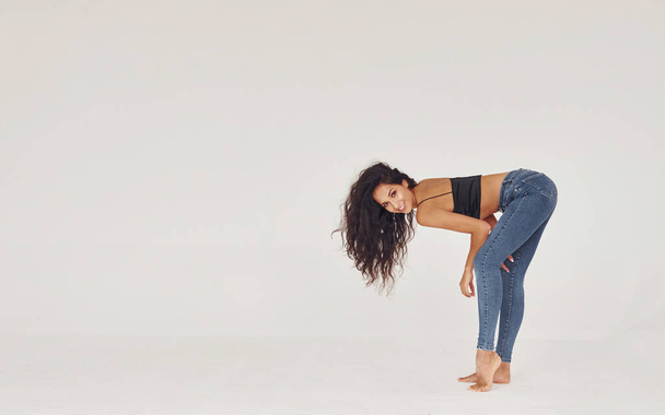 Curly hair. Young woman in jeans and bra indoors. White background. - Foto, Imagen