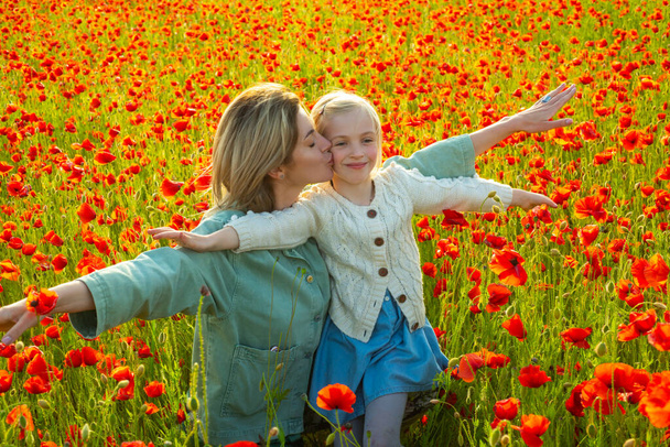 Happy spring family. Carefree mom with a child girl in a field of red poppies enjoys nature. Mother and little daughter in the poppy field. A young woman with her daughter in in a poppy field. - 写真・画像