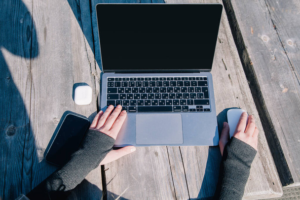 Le mani di una ragazza che lavora su un computer portatile a un vecchio tavolo di legno in natura con il tempo limpido. Vista dall'alto - Foto, immagini