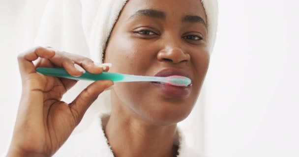 Video of happy african american woman in robe brushing teeth. beauty treatment and skin care routine concept. - Filmati, video