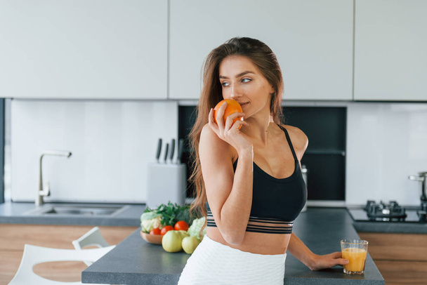 Fresh orange. Young european woman is indoors at kitchen indoors with healthy food. - Foto, Imagen