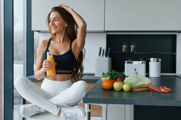 With fresh orange juice. Young european woman is indoors at kitchen indoors with healthy food. - Foto, Imagem