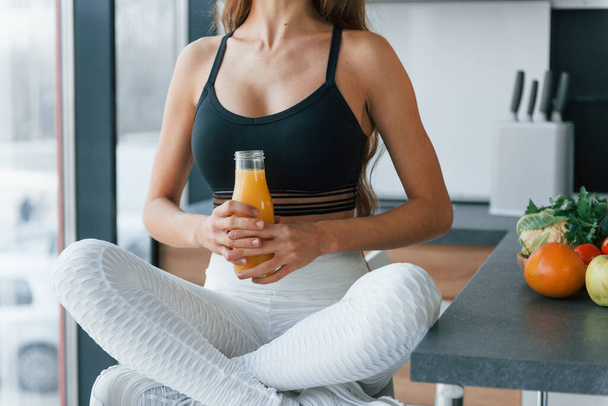With fresh orange juice. Young european woman is indoors at kitchen indoors with healthy food. - Foto, afbeelding