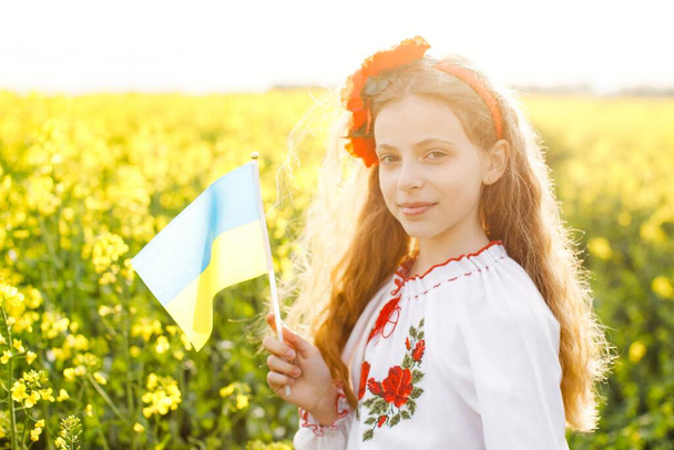 Pray for Ukraine. Child with Ukrainian flag in rapeseed field. Little girl holding national flag in her hand. - Photo, image