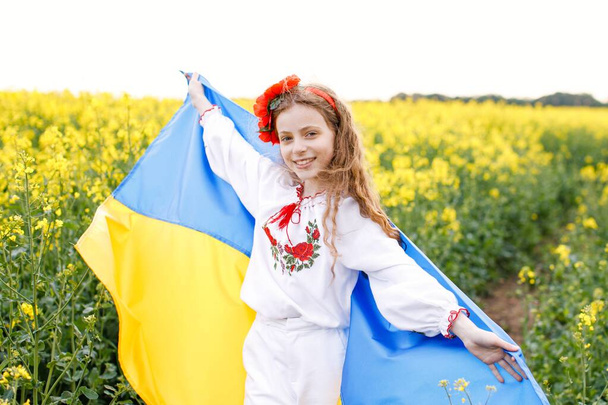 Pray for Ukraine. Child with Ukrainian flag in rapeseed field. Girl holding national flag praying for peace. - Photo, Image