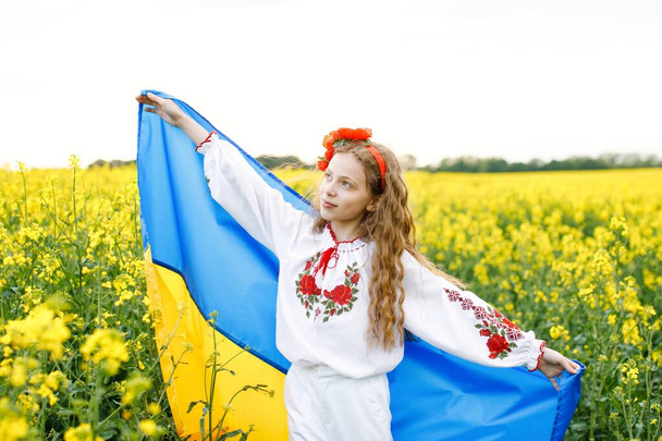 Pray for Ukraine. Child with Ukrainian flag in rapeseed field. Girl holding national flag praying for peace. - Photo, image