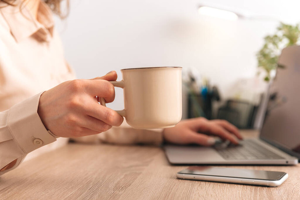 close-up foto van vrouw hand het houden van een keramische kop koffie in kantoor. - Foto, afbeelding