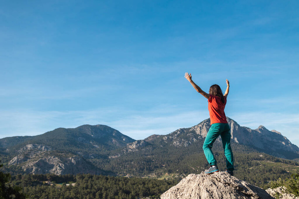Молодая женщина взобралась на вершину горы и подняла руки вверх, путешествуя по горам, добившись успеха в достижении цели - Фото, изображение