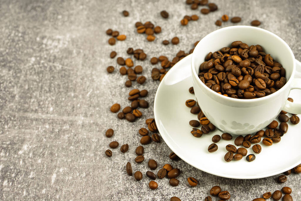 Weiße Kaffeetasse mit gerösteten Kaffeebohnen auf grauem Betonboden mit Kopierraum. - Foto, Bild