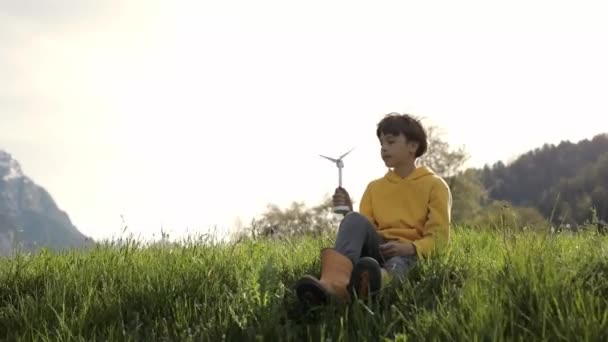 Boy dressed in yellow hoodie keeps model wind turbine. - Video