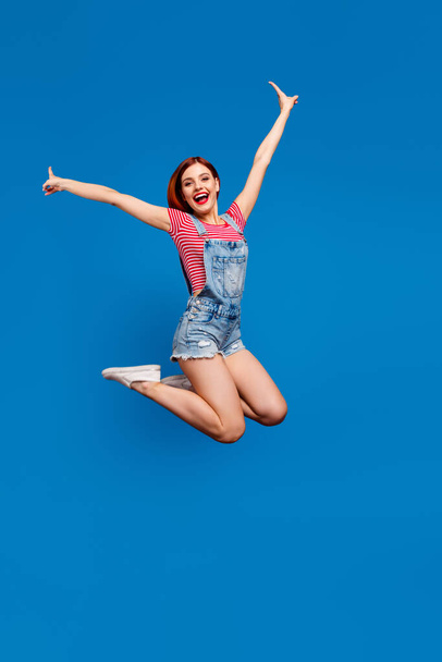 Vertical photo of funky excited young lady dressed denim clothes jumping high rising arms hands isolated blue color background - Foto, Imagem
