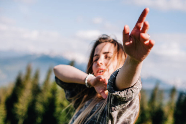 a young, slender girl with loose hair in a plaid shirt and jeans poses for sunny weather in the mountains - Foto, afbeelding