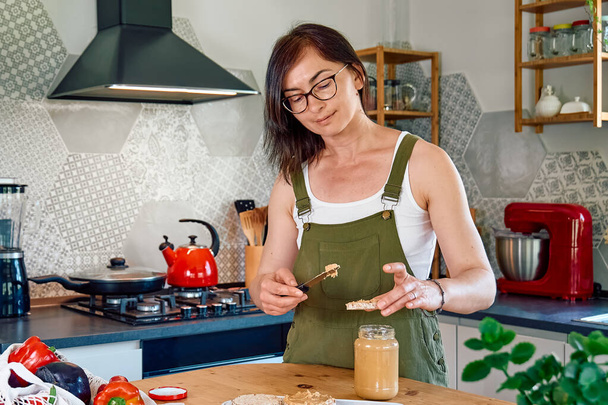 Frau macht gesundes Frühstück oder Brunch und verteilt Erdnussbutter auf einem gepufferten Maiskuchen. Proteindiät gesundes Ernährungskonzept. - Foto, Bild