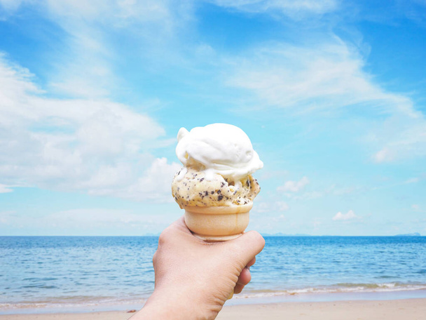 Женщина держит мороженое на фоне летнего пляжа. - Фото, изображение