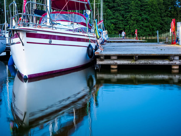 view of bow of moored sailboat near old wooden jetty in a port on a lake, calm summer dusk view - Foto, Imagem