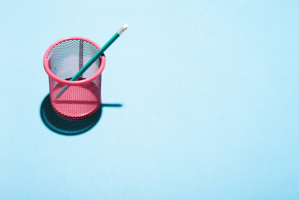Minimal still life image of a mesh pink pencil cup on blue background. - Photo, Image
