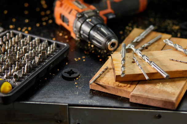 Cierre de un conjunto de brocas metálicas en el taller, el carpintero elige un taladro para perforar un bloque de madera. - Foto, Imagen