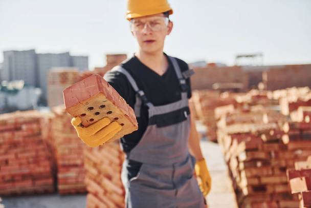 Holds brick in hand. Construction worker in uniform and safety equipment have job on building. - Foto, imagen