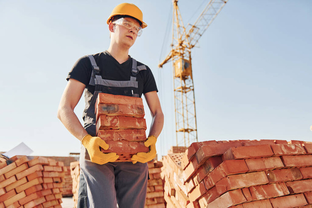 Installing brick wall. Construction worker in uniform and safety equipment have job on building. - Фото, изображение