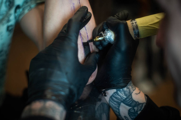 обрезанный снимок процесса татуировки под рукой в салоне. Профессиональный татуировщик вводит чернила в кожу с помощью иглы от татуировки.Профессиональный татуировщик работает в студии. - Фото, изображение