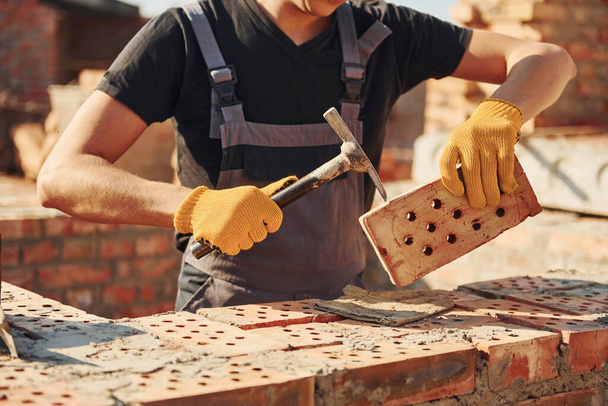 Holding brick and using hammer. Construction worker in uniform and safety equipment have job on building. - Foto, immagini