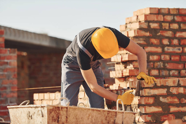 Busy with brick wall. Construction worker in uniform and safety equipment have job on building. - Фото, изображение