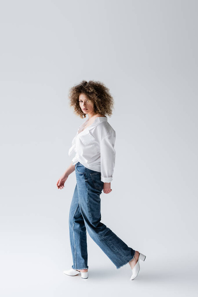 Trendy woman in jeans walking on white background  - Zdjęcie, obraz