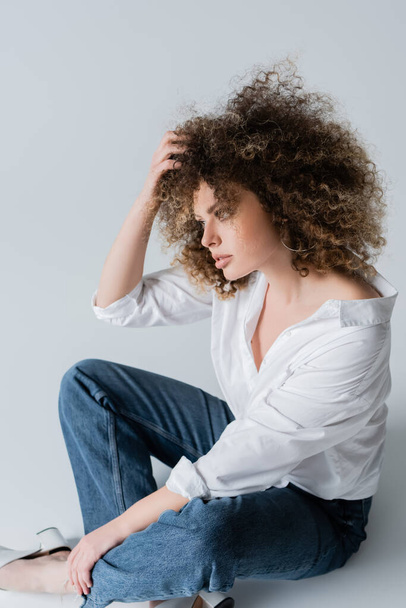 Pretty curly woman in blouse touching hair on white background  - Fotografie, Obrázek