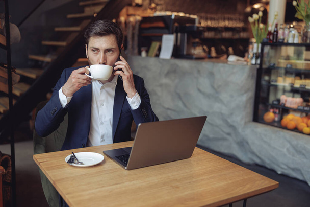 Attractive successful male speaking on cellphone and drinking coffee. Business style. - Photo, Image