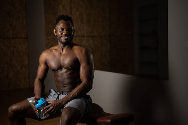 Shirtless african american man drinking from a shaker in the gym. - Foto, Bild
