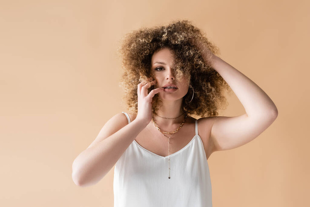 Young woman in white top touching curly hair isolated on beige  - 写真・画像