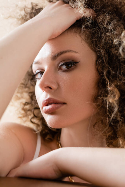 Portrait of young stylish model touching curly hair isolated on beige  - Foto, imagen