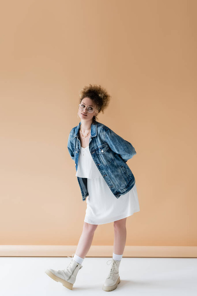 Full length of trendy model in denim jacket standing on beige background  - Fotoğraf, Görsel