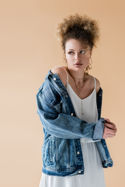 Curly woman in denim jacket looking away isolated on beige  - Photo, Image
