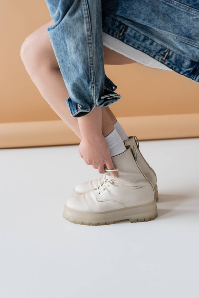 Cropped view of young woman touching stylish boots on beige background - Foto, Imagem