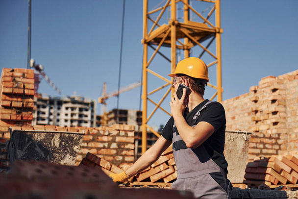 Talking by phone. Construction worker in uniform and safety equipment have job on building. - Foto, Imagem