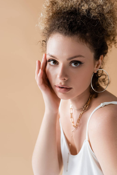 Portrait of curly model in accessories touching face isolated on beige  - Valokuva, kuva