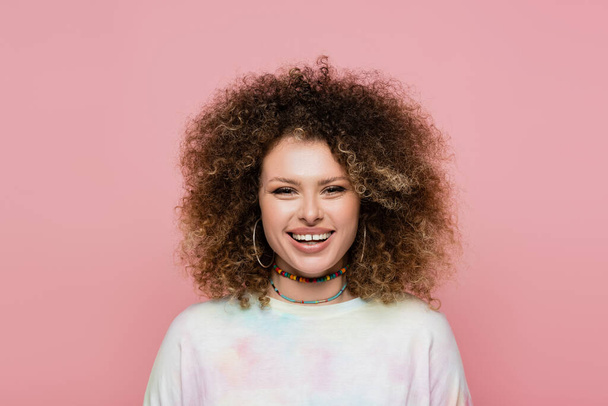 Cheerful curly woman looking at camera isolated on pink  - Фото, зображення