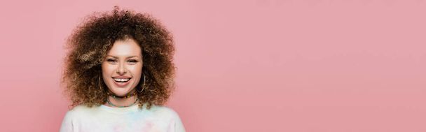 Positive curly model looking at camera isolated on pink, banner  - 写真・画像