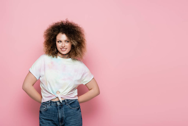 Smiling curly woman in t-shirt looking away on pink background - Foto, Imagem