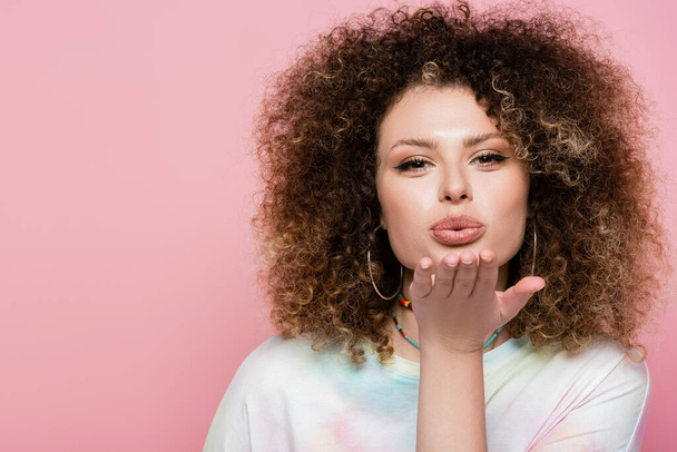 Portrait of young curly woman blowing air kiss isolated on pink  - Foto, Imagem