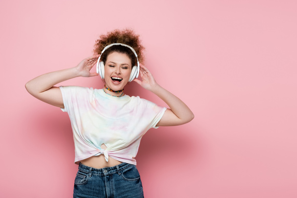 Positive woman in headphones singing on pink background - Foto, Bild