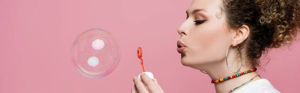 Curly woman blowing soap bubble on pink background, banner  - Photo, Image