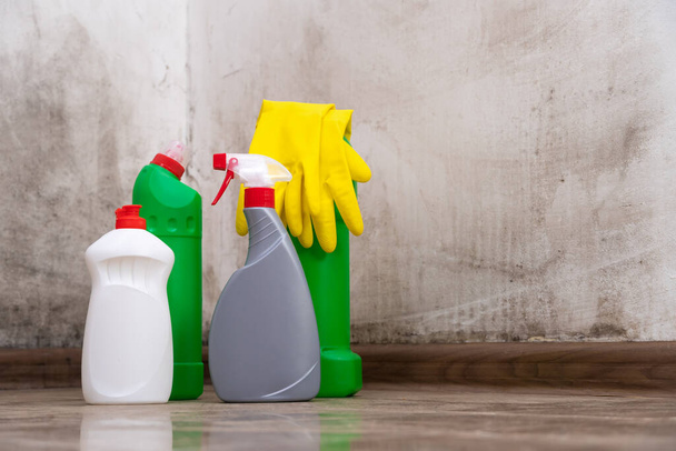 床に立つ洗浄製品のクローズアップ、壁から型を除去するための黄色の手袋。掃除、家事の概念 - 写真・画像