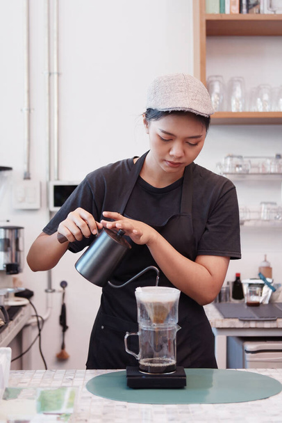 Uśmiechnięta Azjatka Młoda baristka nosi fartuch i parzy kawę z ekspresem do zamawiania przez klientów w kawiarni i kawiarni. Rozpocznij działalność w małej kawiarni i technologii Concept. - Zdjęcie, obraz