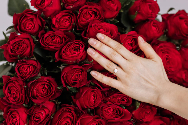 sagte sie ja. Nahaufnahme der Hand einer Frau mit Verlobungsringen. Hand der auf dem Hintergrund des großen Straußes roter Rosen. Romantische Antragszeit. - Foto, Bild