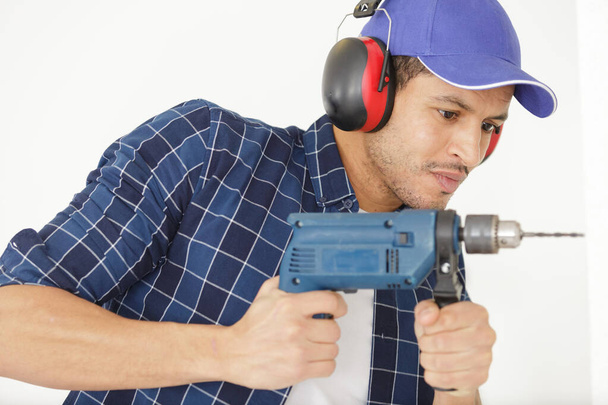 builder with electric drill making hole in wall - Foto, imagen