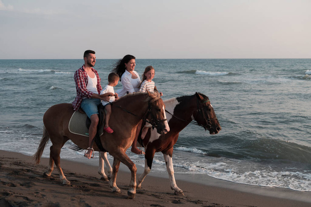 The family spends time with their children while riding horses together on a beautiful sandy beach on sunet.  - Photo, image